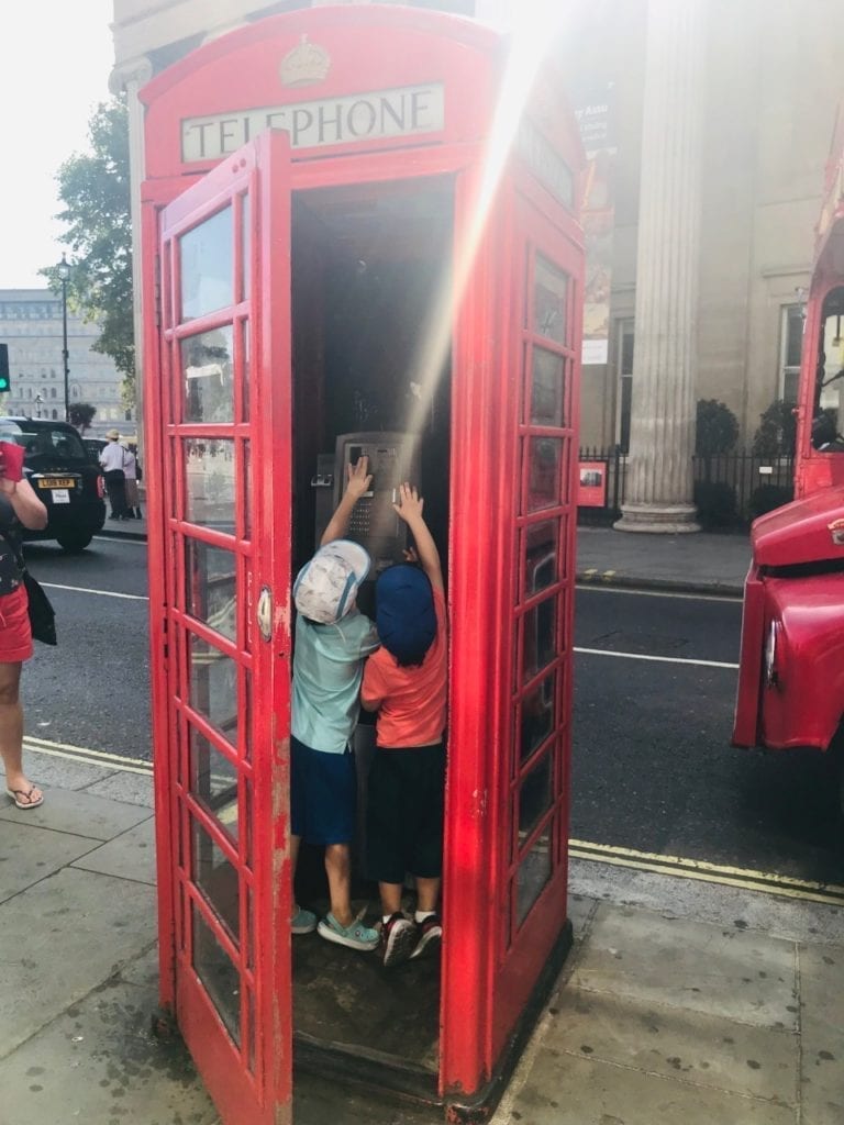 travel tips for traveling to europe with toddlers  - Two boys playing with a phone in a red telephone booth in London, England