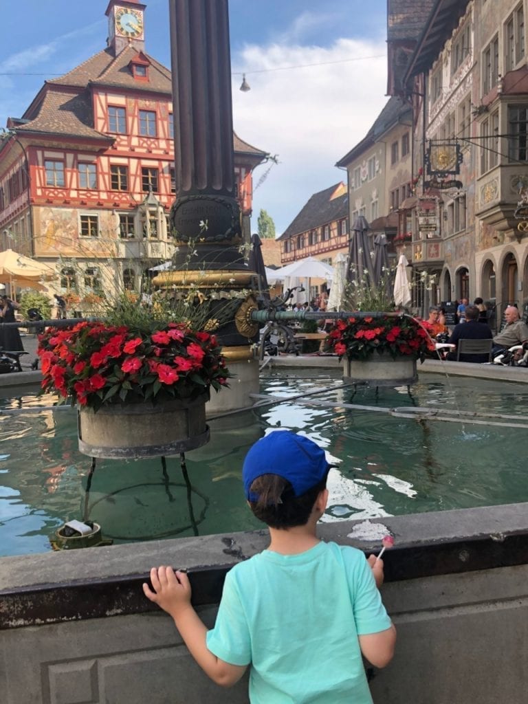 travel tips for traveling to europe with toddlers  - A boy looking at the fountain with flowers in a medieval town of Stein am Rhine in Switzerland